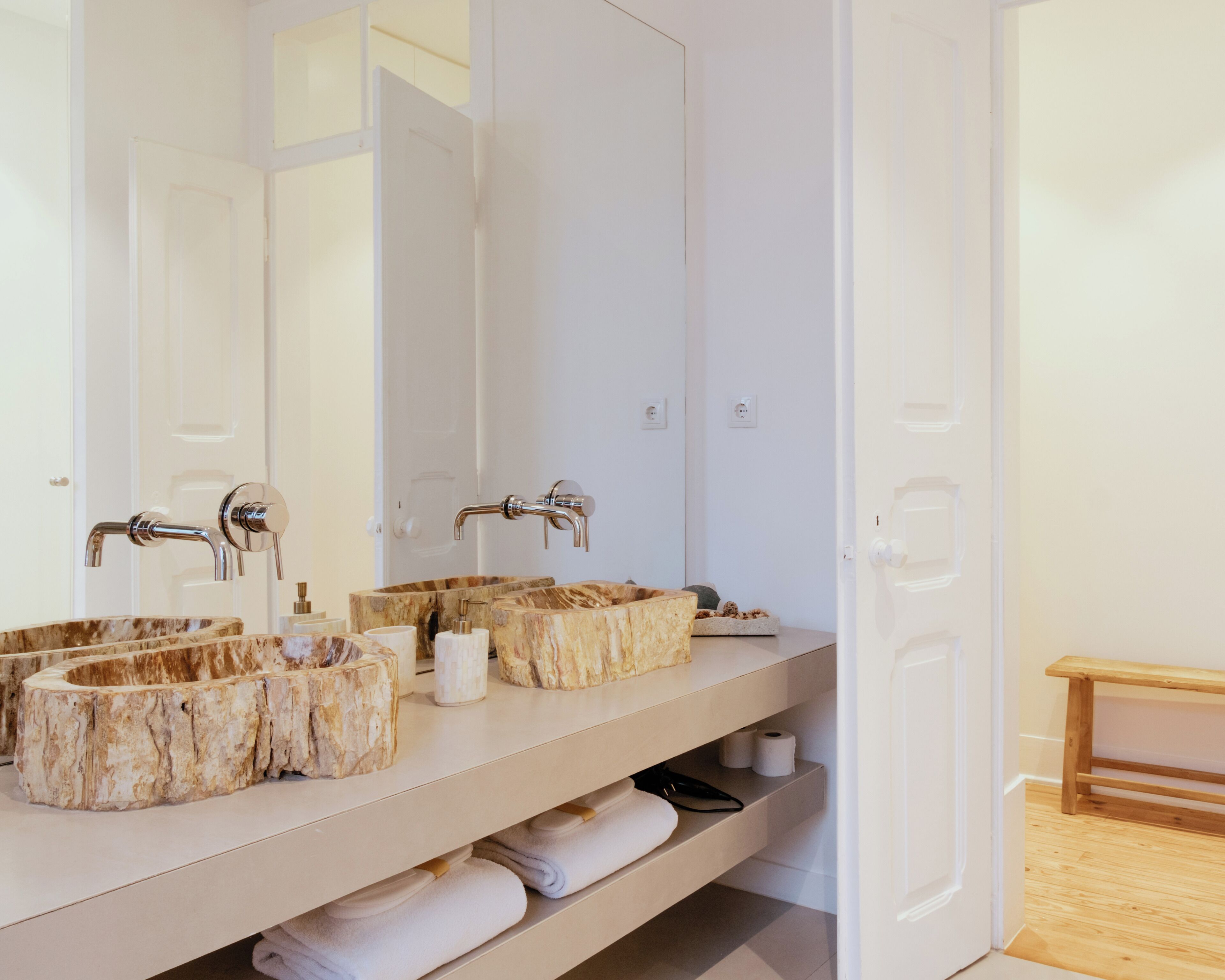 Un baño con dos lavamanos, cada uno con una pila de piedra única, un espejo grande y un banco de madera.