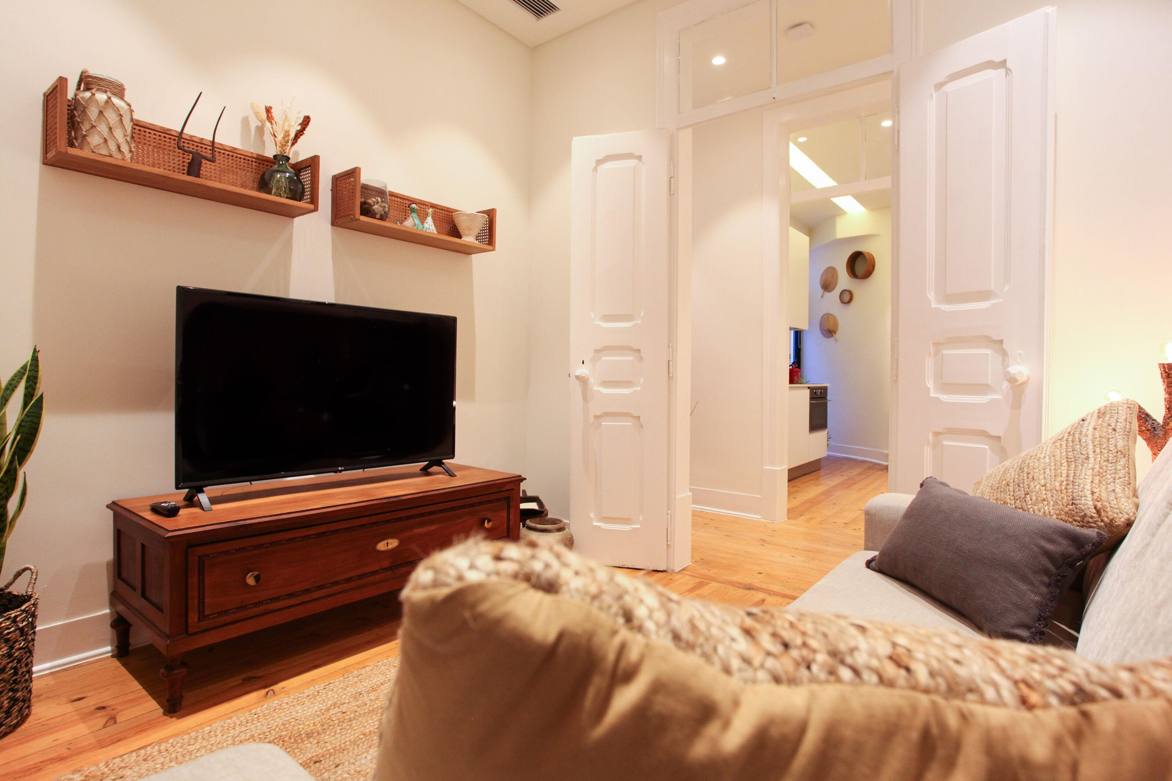 Uma sala de estar com televisão sobre um armário de madeira, um sofá e uma porta que dá para outro cômodo.