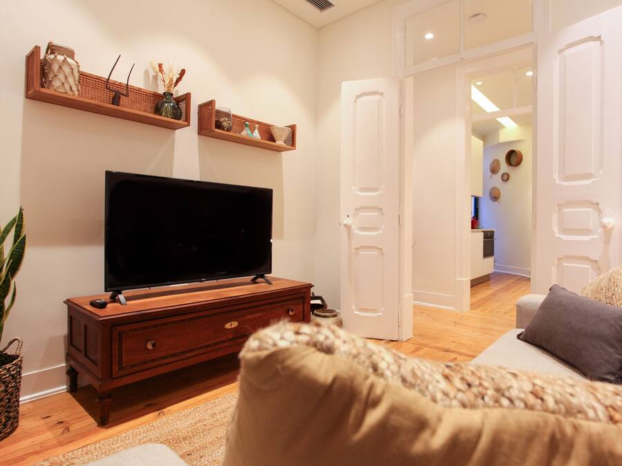 Uma sala de estar com televisão sobre um armário de madeira, um sofá e uma porta que dá para outro cômodo.