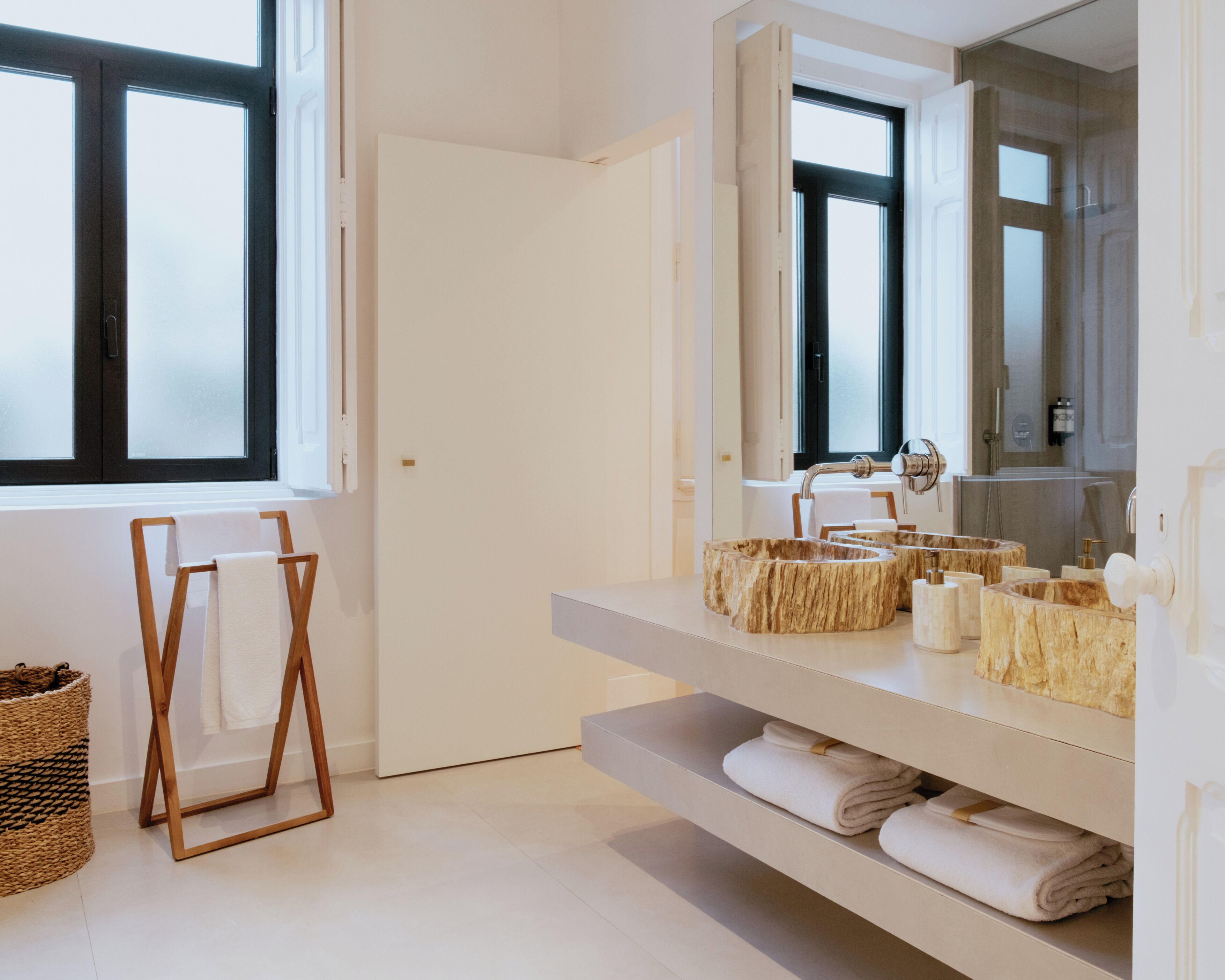 A modern bathroom with a large mirror, a sink with a unique wood-like basin, and neatly folded towels on shelves.