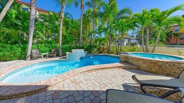 Una piscina con borde de piedra, rodeada de palmeras y un patio de ladrillo.