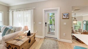Una sala de estar con sofá, mesa de centro, puerta y comedor con mesa y sillas.