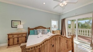 Un dormitorio con cama de madera, mesita de noche, ventilador de techo y vistas al exterior.