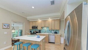Una cocina moderna con una isla central, taburetes de bar, electrodomésticos de acero inoxidable y armarios de madera.