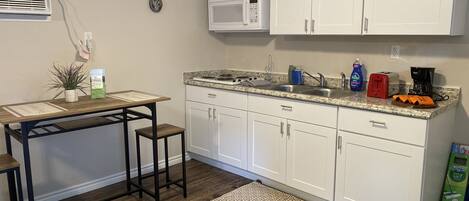 A kitchen with white cabinets, a microwave, a sink, a coffee maker, and a table with stools.