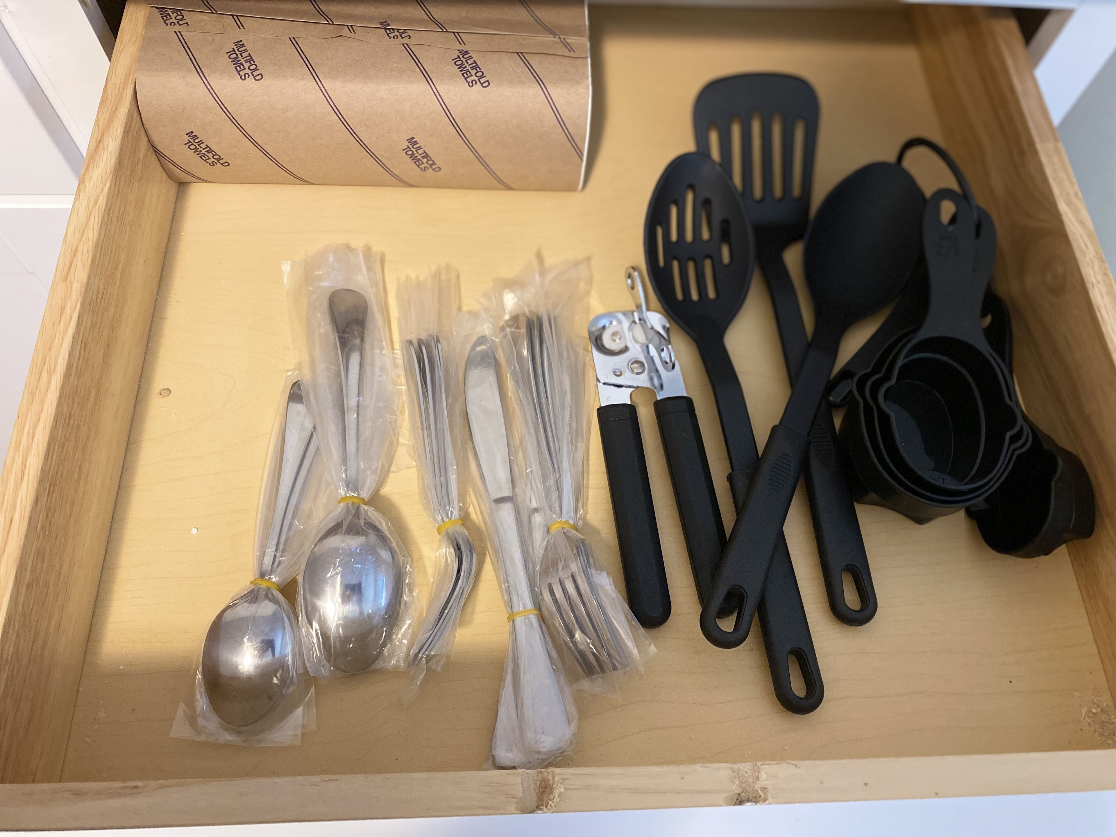 Un tiroir contenant un ensemble d’ustensiles de cuisine, notamment des cuillères, des fourchettes, des spatules et des tasses à mesurer, le tout emballé avec soin.
