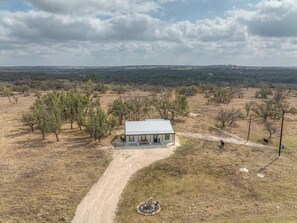 Una casa de un solo piso con techo de metal, rodeada por un paisaje árido con pocos árboles.