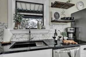 A modern kitchen with a marble backsplash, a stainless steel sink, a coffee machine, and a window with a view of trees. - Hill Country-Fire Pit & Hot Tub! (Fredericksburg)