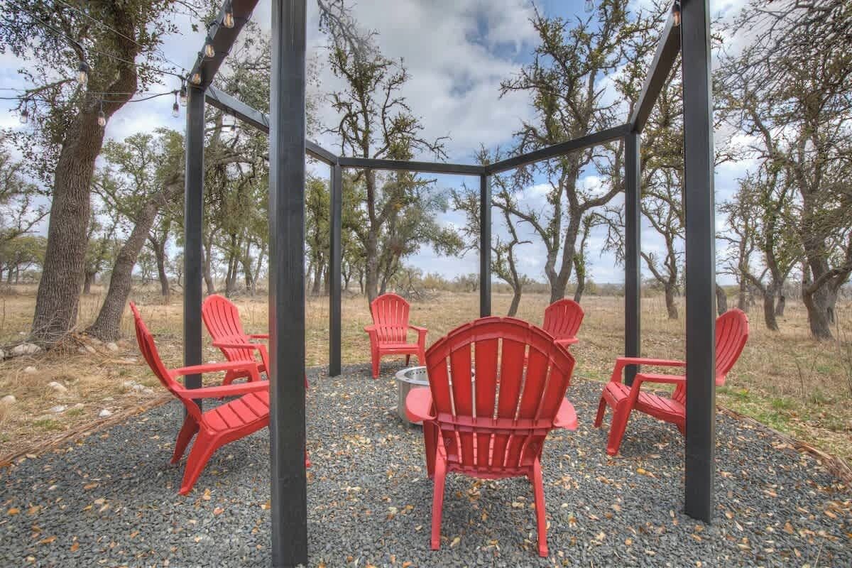 A gazebo with red chairs and a table, surrounded by trees and gravel.