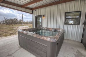 Un jacuzzi en un área exterior techada con vista a árboles y un cielo nublado.