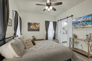 A bedroom with a bed, a ceiling fan, a painting, a window with curtains, and a TV on a stand. - Hill Country-Fire Pit & Hot Tub! (Fredericksburg)