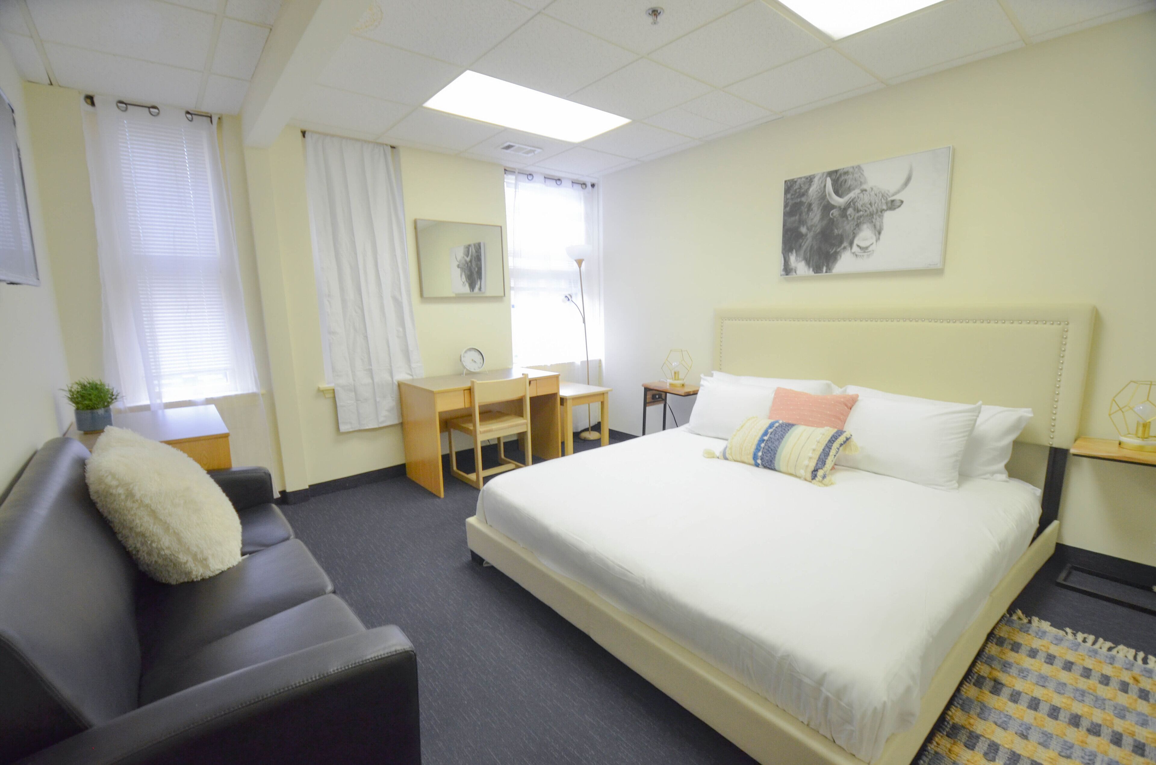Ein Hotelzimmer mit Bett, Schreibtisch, Stuhl, Sofa und einem Fenster mit Vorhängen.