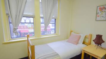 A small, neatly arranged bedroom with a single bed, a bedside table, and a window with curtains.