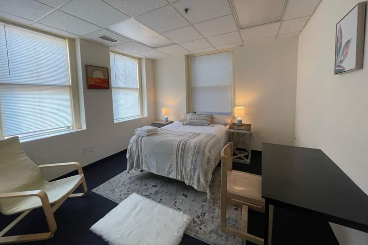 A bedroom with a bed, bedside tables, a desk, a chair, and a window.