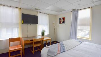 Ein Hotelzimmer mit Bett, Schreibtisch, Stuhl, Fernseher und einem Fenster mit Jalousien.