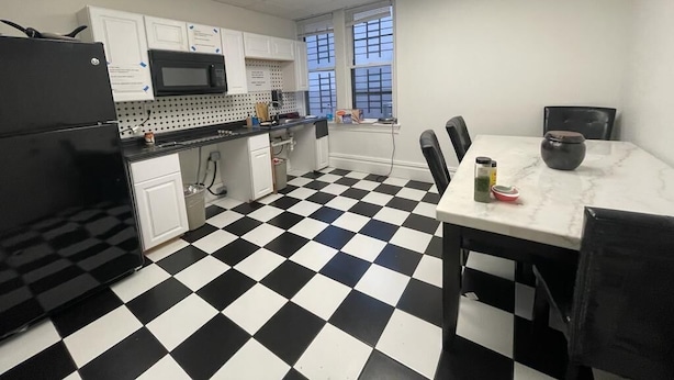 A kitchen with a black and white checkered floor, white cabinets, a microwave, and a dining table with chairs. - Michie House in College Hill - Hostel (Providence)