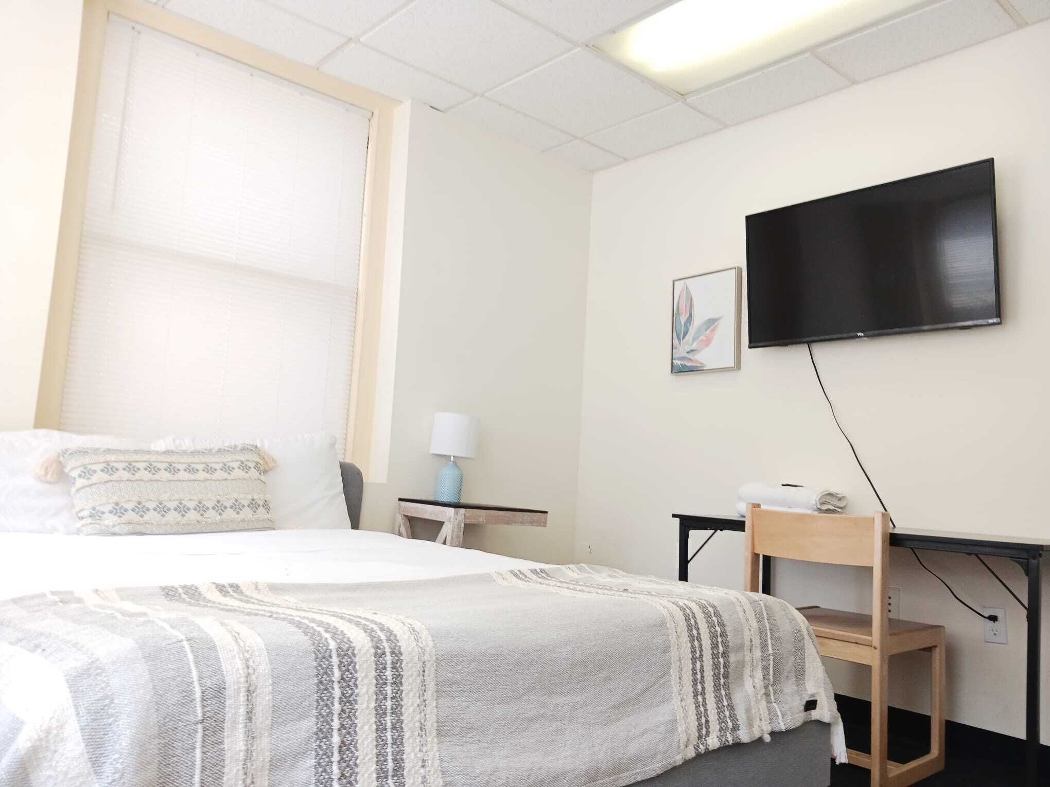 A hotel room with a bed, a desk, a chair, a television, and a window with blinds.