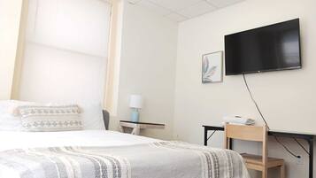 A hotel room with a bed, a desk, a chair, a television, and a window with blinds.
