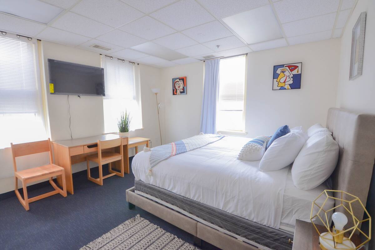 A bedroom with a bed, desk, chair, and a TV on the wall.