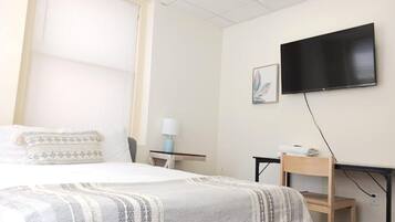 A hotel room with a bed, a desk, a chair, a TV, and a window with blinds.