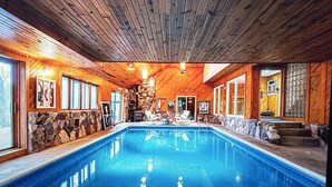 A large indoor swimming pool with wooden walls and stone accents, surrounded by lounge chairs and a stone fireplace. - Road America Adjacent Lake House with indoor pool (Plymouth)