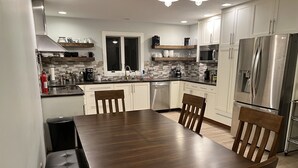 A modern kitchen with white cabinets, a stainless steel refrigerator, a microwave, and a dining table with chairs. - Road America Adjacent Lake House with indoor pool (Plymouth)