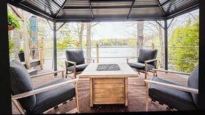 A covered outdoor seating area with a table and chairs, overlooking a body of water. - Road America Adjacent Lake House with indoor pool (Plymouth)