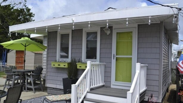 Una casa pequeña con porche, mobiliario exterior y una puerta verde.