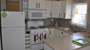 Una cocina compacta con alacenas blancas, un microondas, una estufa a gas y un lavamanos.