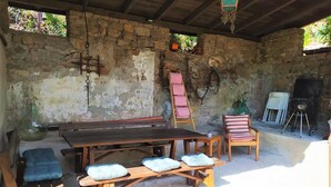 Une terrasse extérieure avec une table en bois, deux chaises rembourrées, un banc en bois et un barbecue.