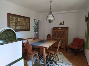 A dining area with a wooden table and chairs, a zebra-patterned rug, a green hanging lamp, and a framed botanical illustration on the wall.