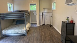 Ein Zimmer mit Etagenbett, Wäscheständer, Kommode und Fenster mit Blick auf Grünflächen.