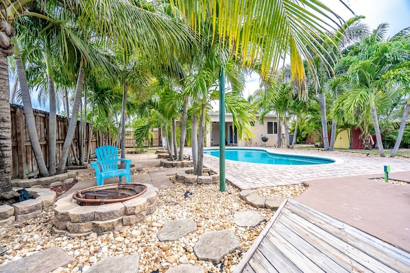 A pool area with a wooden deck, a blue chair, and a stone fire pit.