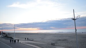 A beach with a few people walking, a bench, and street lamps. - Apartment (Coxyde)