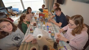 A group of people sitting around a table with various food items and drinks, a bottle of water, and a box of cereal. - Apartment (Coxyde)