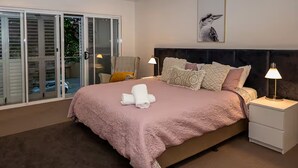 Een slaapkamer met een bed, nachtkastjes, een plafondventilator, een schuifdeur met glas en een ingelijst schilderij aan de muur.