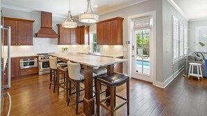 A modern kitchen with wooden cabinets, stainless steel appliances, and a central island with bar stools. - Stella Maris- Updated Home, Heated Private Pool, Walk to the Beach + Gulf Place! (Santa Rosa Beach)