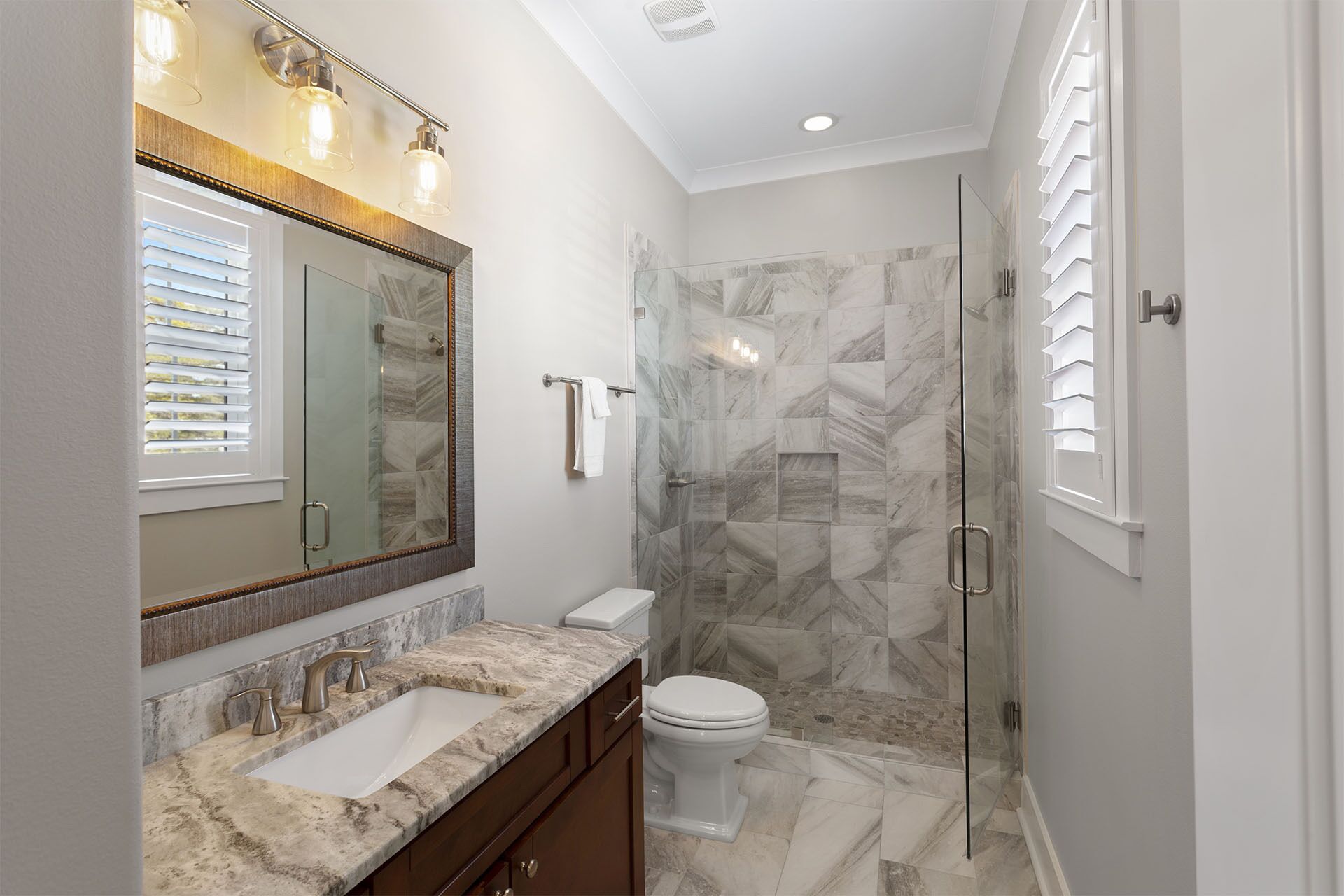 A modern bathroom with a marble sink, a glass-enclosed shower, and a large mirror.