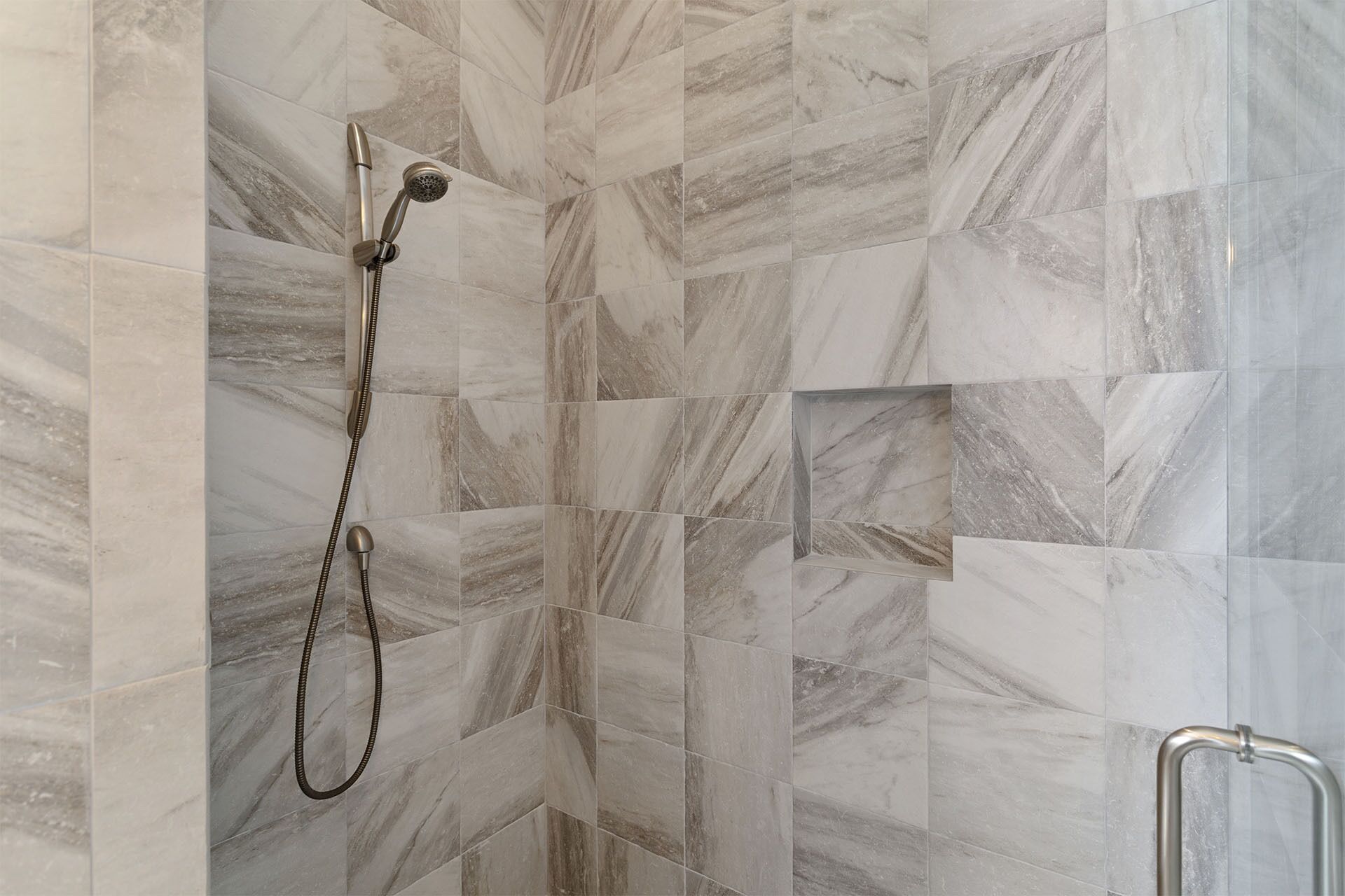A shower area with a handheld showerhead and a wall-mounted handrail.
