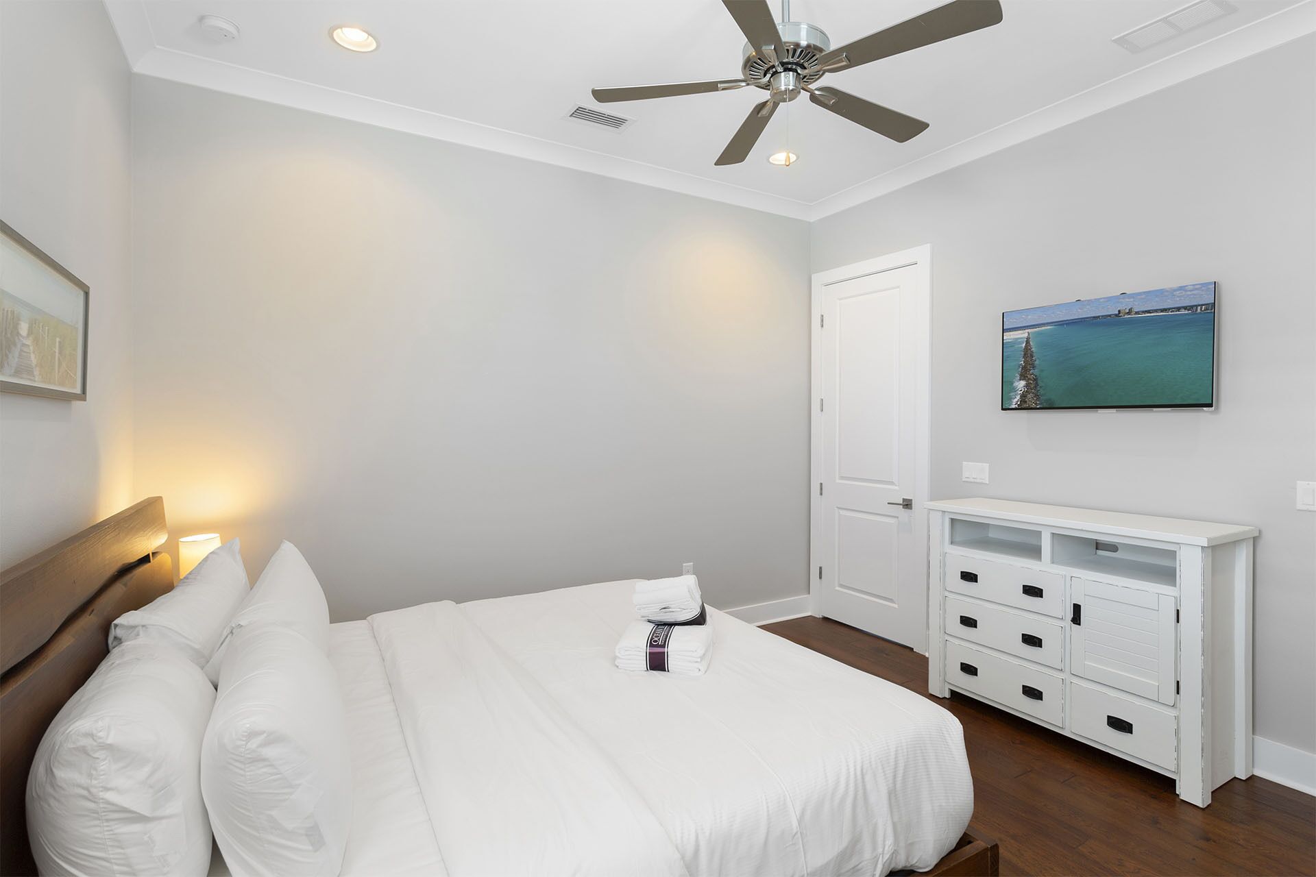 A bedroom with a bed, a ceiling fan, a nightstand, a dresser, and a painting on the wall.