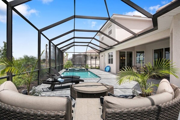 A covered outdoor area with a swimming pool, lounge chairs, and wicker furniture.