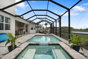 A covered outdoor swimming pool with a patio area, a stone fireplace, and a view of a lake.