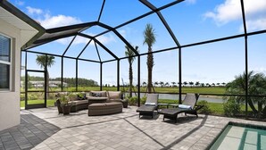 Een overdekt terras buiten met een zwembad, een zithoek en uitzicht op een meer en palmbomen.