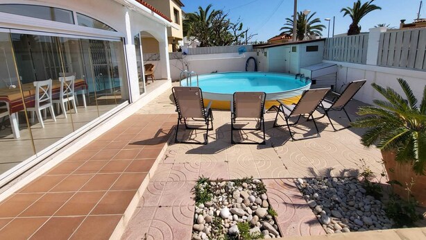A swimming pool with lounge chairs, a glass-enclosed dining area, and a tiled patio. - Charming villa with swimming pool, very well equipped and 900m from the beach (Torredembarra)