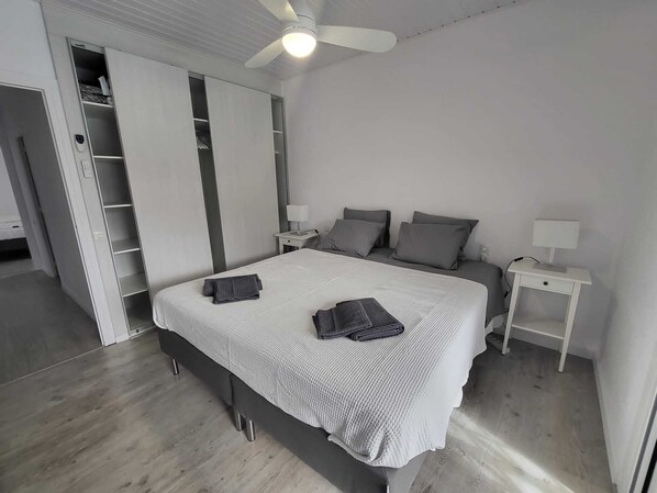 A bedroom with a bed, two bedside tables, a ceiling fan, and a wardrobe with a mirror.