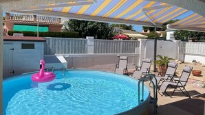 A swimming pool with a pink flamingo float, a covered patio area with lounge chairs, and a white fence surrounding the pool. - Charming villa with swimming pool, very well equipped and 900m from the beach (Torredembarra)