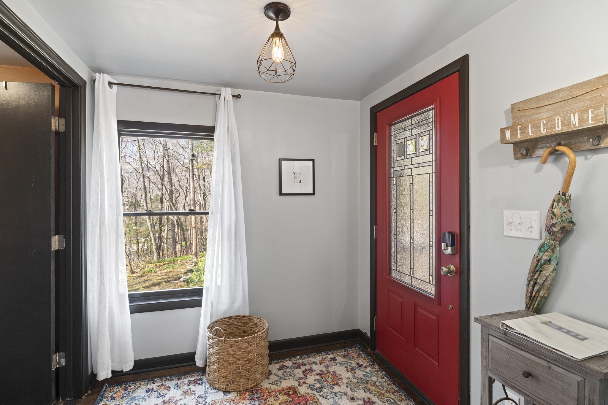 A hallway with a red door, a welcome sign, a wicker basket, and a patterned rug.
