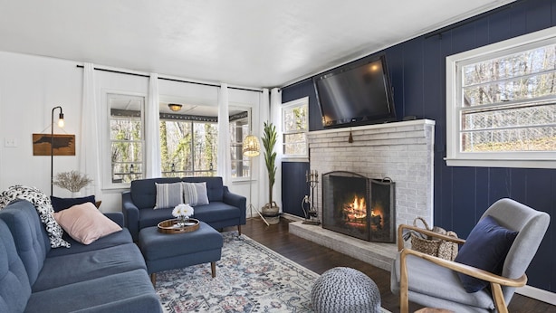 A living room with a fireplace, dark blue walls, and a large window. - Private + Wooded + Quaint & Cozy + 5 mins to Dwntn Blk Mtn + 15 mins to Ashvle (Black Mountain)