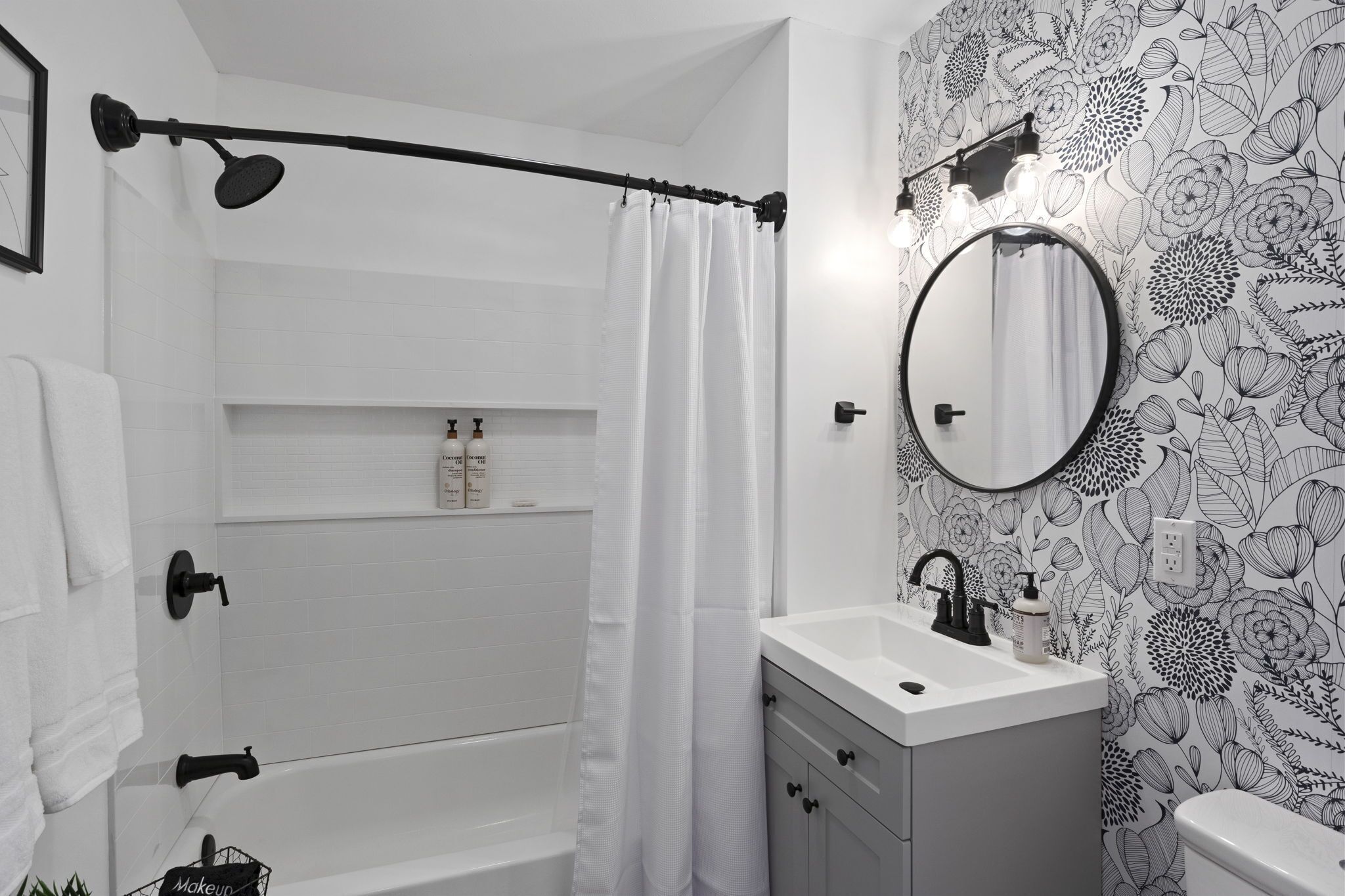 Et badeværelse med badekar, bruseforhæng, vask med spejl og toilet.
