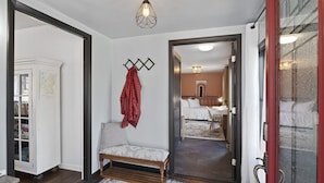 A hallway with a wooden bench, a coat rack with a red jacket, a map on the wall, and a door leading to a bedroom with a bed and a nightstand. - Private + Wooded + Quaint & Cozy + 5 mins to Dwntn Blk Mtn + 15 mins to Ashvle (Black Mountain)